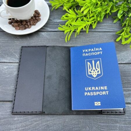 Відкрита чорна шкіряна обкладинка для паспорта з українським паспортом всередині на дерев'яній поверхні.