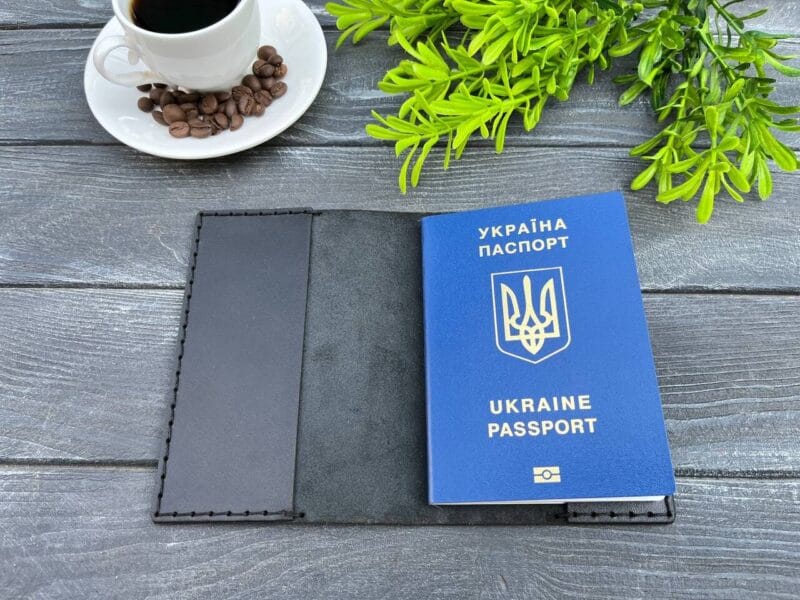 Відкрита чорна шкіряна обкладинка для паспорта з українським паспортом всередині на дерев'яній поверхні.