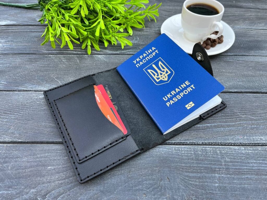 Чорний шкіряний тримач для документів з українським паспортом та банківською карткою на дерев'яному фоні.