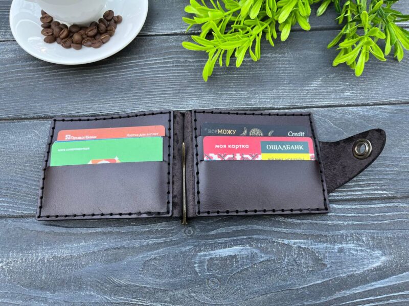 Відкритий коричневий шкіряний затискач для купюр із картками у внутрішніх слотах, розміщений на дерев'яній поверхні.