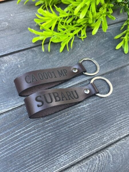 Коричневі шкіряні брелоки з гравіюванням "CA 0001 MP" та "SUBARU".