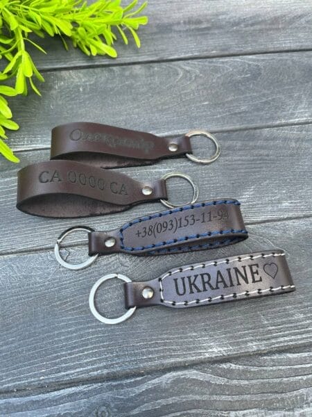 Шкіряні брелоки з різними гравіюваннями, включаючи імена, автомобільні номери та патріотичні написи.