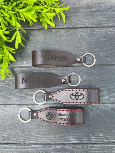 Чотири шкіряних брелоки з написами та логотипами (Roman, Nissan, Toyota та Volkswagen) на дерев'яній поверхні.