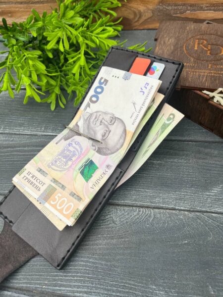 Відкритий шкіряний гаманець із вставленими купюрами номіналом 500 гривень, розташований на дерев'яній поверхні з декоративною зеленою рослиною та дерев'яною коробкою на задньому плані.