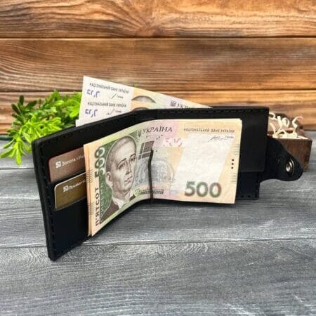 Відкритий чорний гаманець із вкладеними купюрами номіналом 500 гривень і картками, розташований на дерев'яній поверхні з декоративною зеленню на задньому плані.