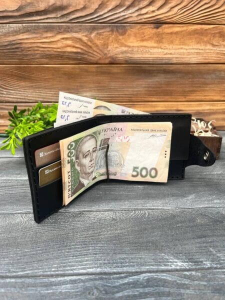 Відкритий чорний гаманець із вкладеними купюрами номіналом 500 гривень і картками, розташований на дерев'яній поверхні з декоративною зеленню на задньому плані.